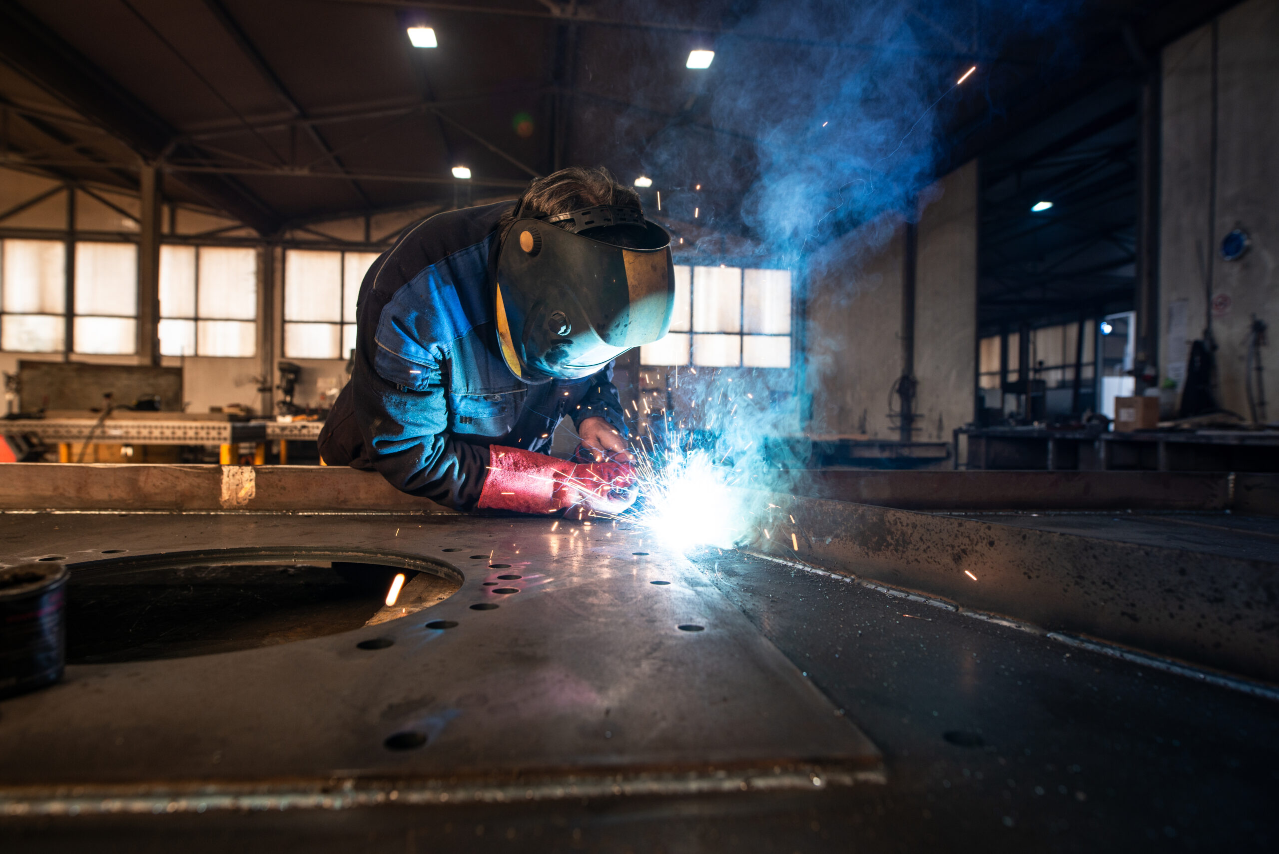 Professional industrial welder welding metal parts in metalworking factory.